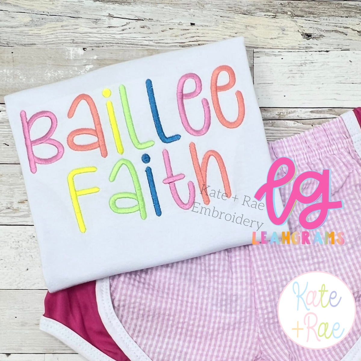 Happy Days Satin Stitch Embroidery Font: The name Baillee Faith in pastel satin stitch letters on a white shirt with pink gingham shorts