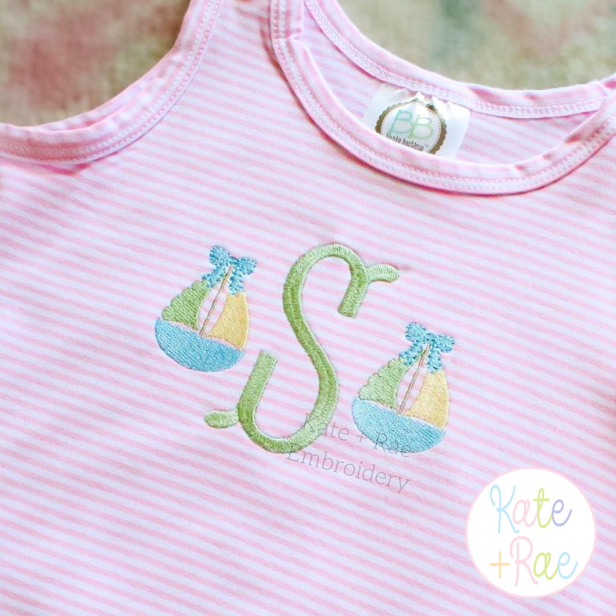 Girl's Sailboat with Bow Mini Fill Stitch Embroidery Design: Two mini sailboats with blue bows beside a green letter S on a pink striped shirt