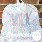Beau Fill Stitch with Satin Border Embroidery Font: The name MILA in pink and blue fill stitch letters on a floral backpack