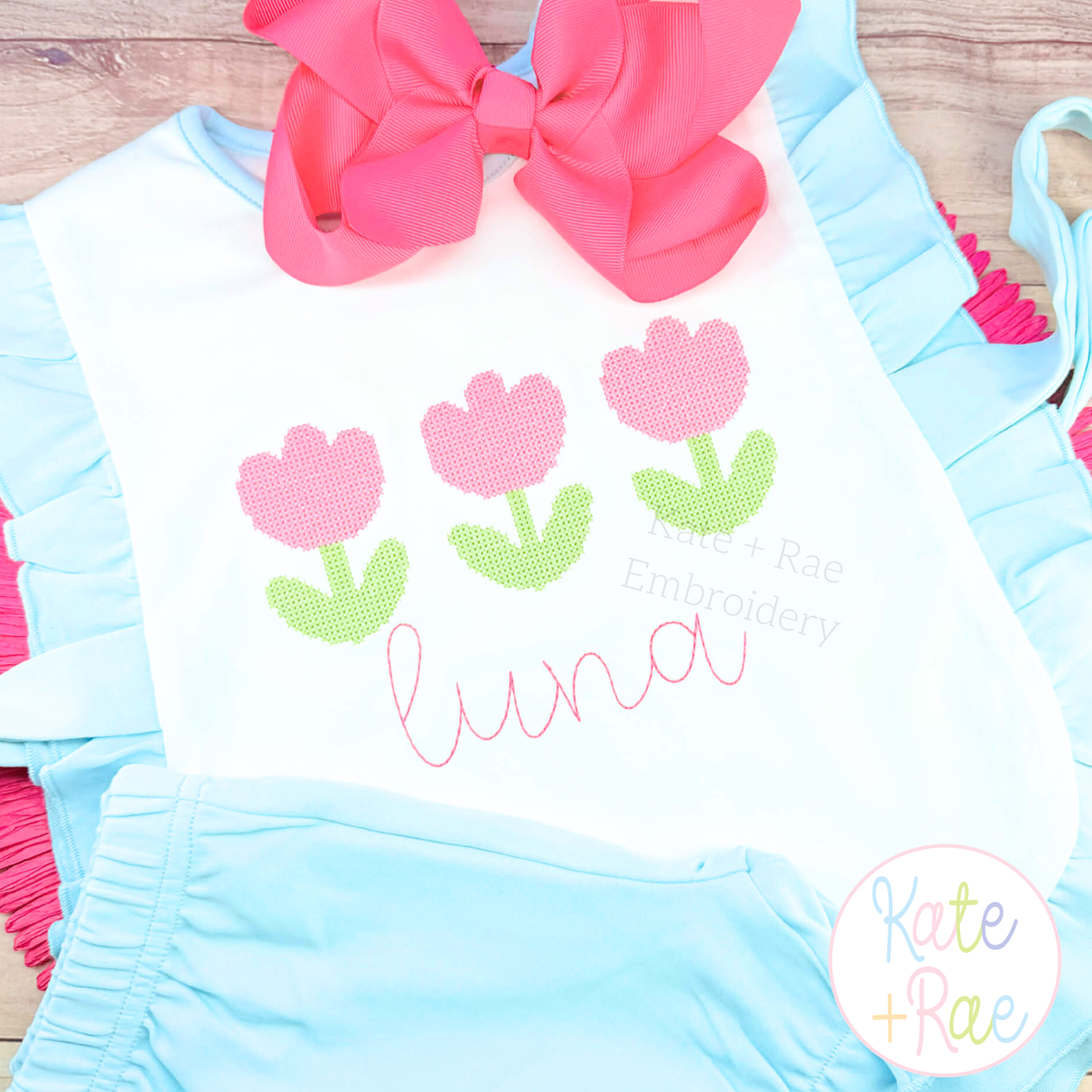 Mini Tulip Trio Cross Stitch Embroidery Design: Three pink cross stitch tulips above the name luna in pink script on a white ruffle romper