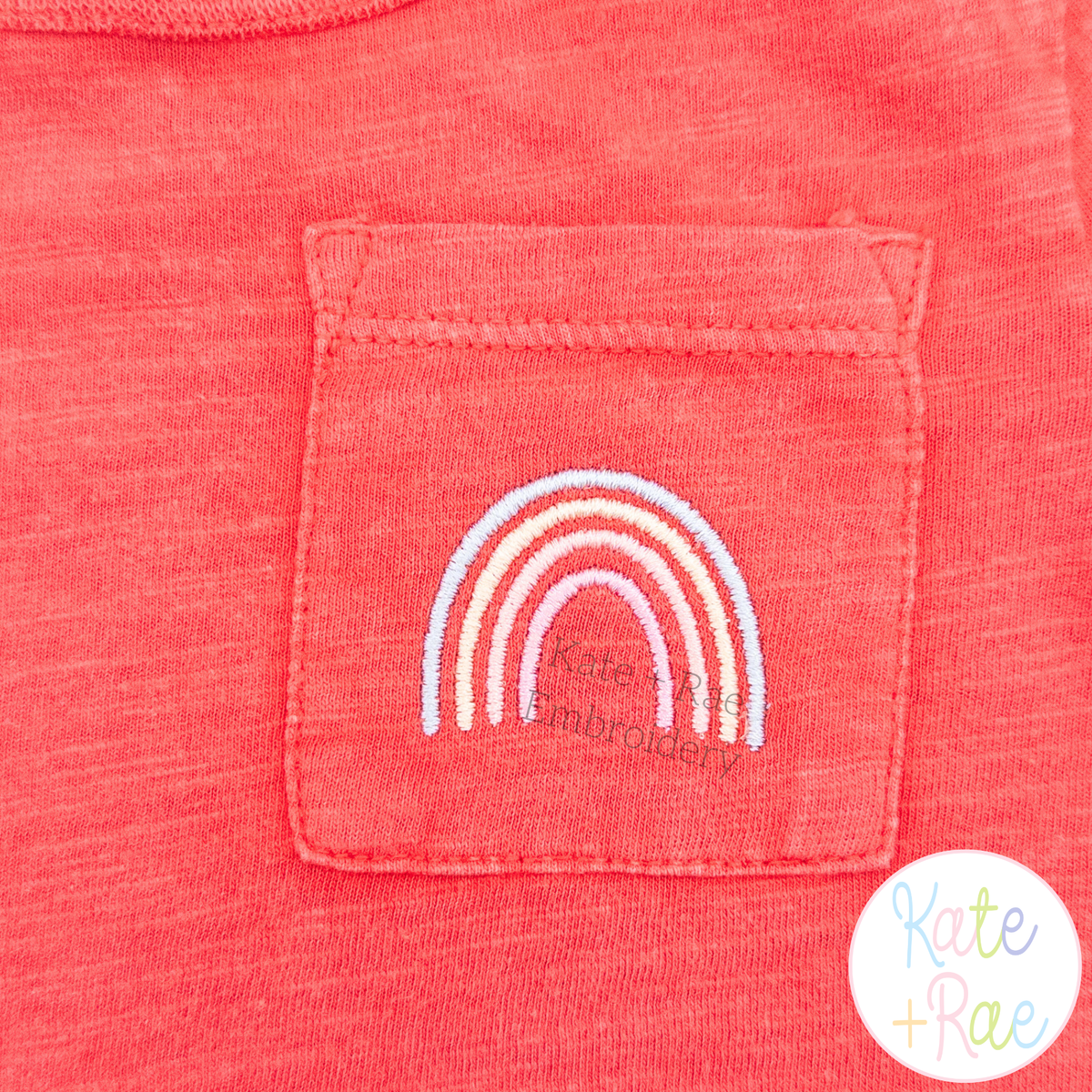 Rainbow Mini Fill Embroidery Design: Small pastel rainbow embroidered on the pocket of a coral tee