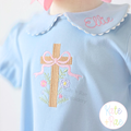 Floral Cross Pattern Fill Stitch Embroidery Design: Tan fill stitch cross with a pink bow and flowers on a light blue shirt with the name Ellie on the collar