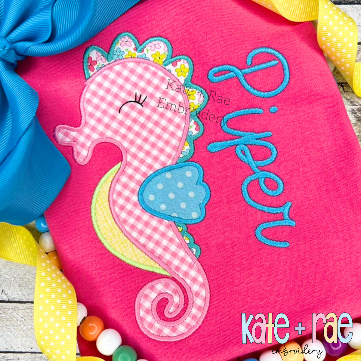 Seahorse Satin Stitch Applique Embroidery Design: Pink gingham seahorse applique beside the name Piper in blue script on a hot pink shirt