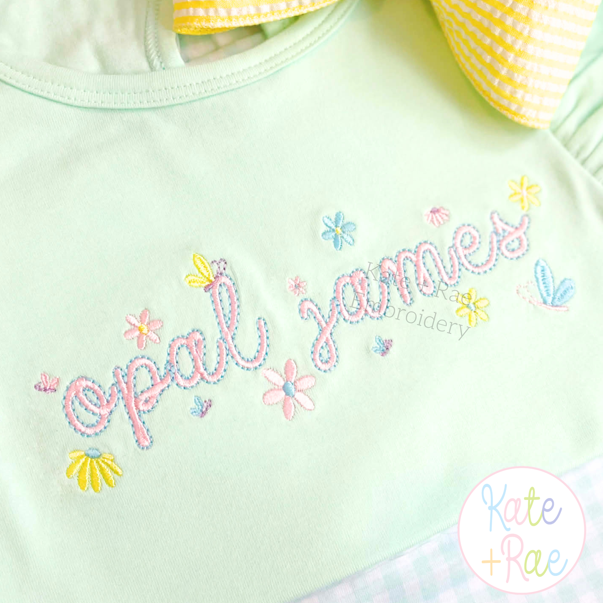 The name opal james in pink outline script with tiny flowers on a mint shirt