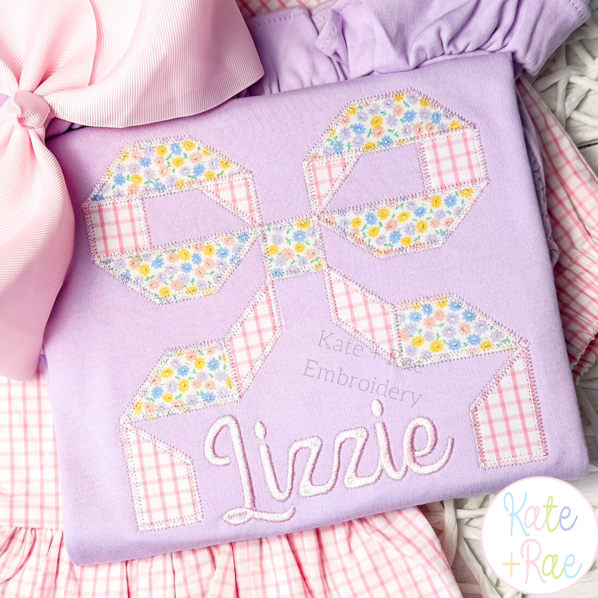 Quilt Block Bow 2 Zigzag Applique Embroidery Design: Floral and gingham quilt block bow applique above the name Lizzie in lavender script on a purple shirt