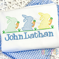 Boy's Easter Bunny with Carrots Trio Cross Stitch Embroidery Design: Three green, blue, and yellow cross stitch bunnies holding carrots above the name John Lathan in blue on a white shirt