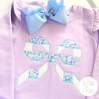 Quilt Block Bow Zigzag Applique Embroidery Design: Blue and white floral quilt block bow applique on a lavender ruffle shirt