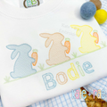 Boy's Easter Bunny with Carrots Trio Sketch Stitch Embroidery Design: Three blue, tan, and yellow sketch bunnies holding carrots above the name Bodie in pastel letters on a white shirt