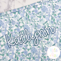 Hello Outline Satin Stitch Embroidery Font: The name Katlynn in navy outline satin script on a blue floral bag