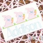 Girl's Easter Bunny with Carrots Trio Cross Stitch Embroidery Design: Three pink cross stitch bunnies with blue bows holding carrots above the name Addison in light blue on a white shirt