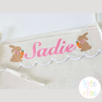 Girl's Easter Bunny with Carrot and Bow Mini Fill Stitch Embroidery Design: Two brown mini bunnies with carrots beside the name Sadie in pink script on a scalloped basket liner