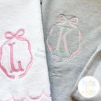 Emma Long Tail Monogram Bow Satin Stitch with Bean Outline Embroidery Design: Pink bow frames around letters L and K on white and gray sweatshirts