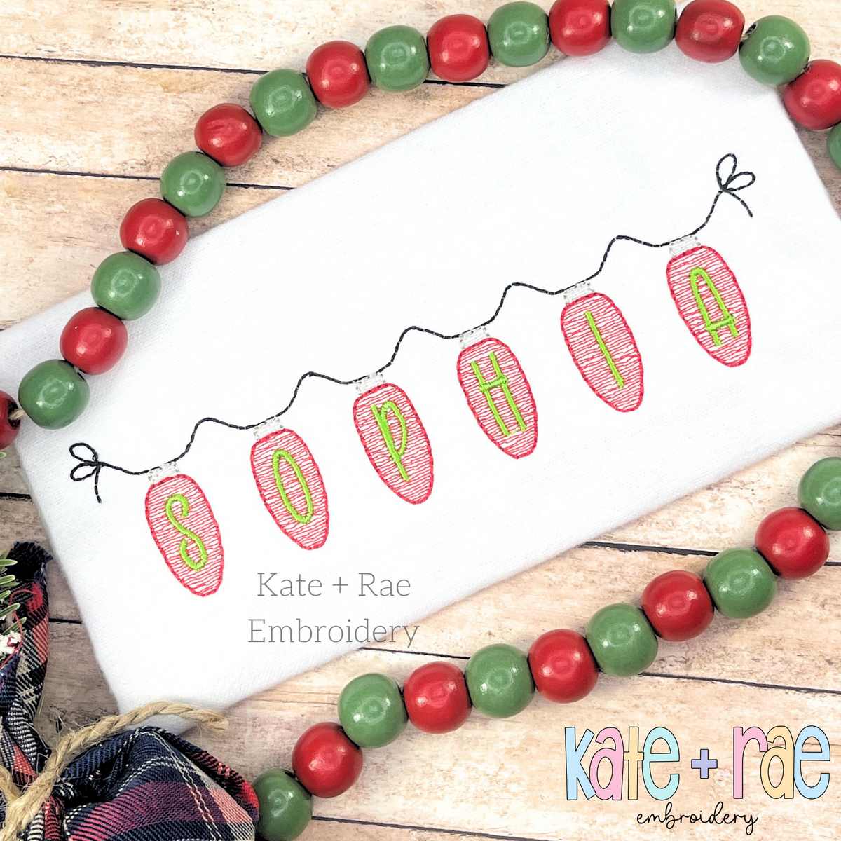 Christmas Lights Sketch Stitch Applique Embroidery Font: Pink sketch stitch Christmas light bulbs spelling SOPHIA on a strand on a white shirt