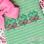 Shamrock Trio with Connecting Bows Sketch Stitch Embroidery Design: Three green sketch stitch shamrocks linked by pink bows on a green textured shirt