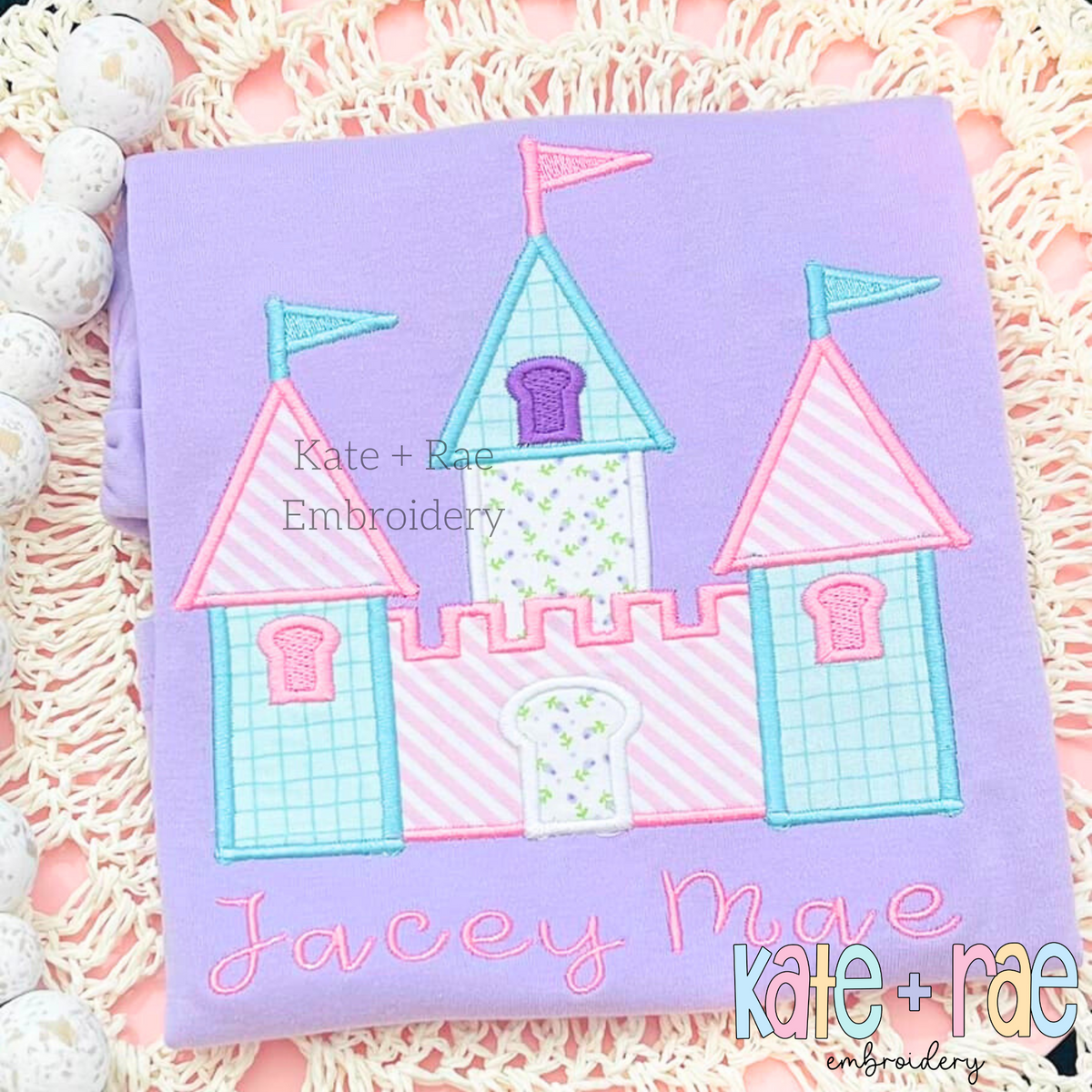 Princess Castle Satin Stitch Applique Embroidery Design: Princess castle applique in pastel gingham and stripes above the name Jacey Mae in pink script on a lavender shirt