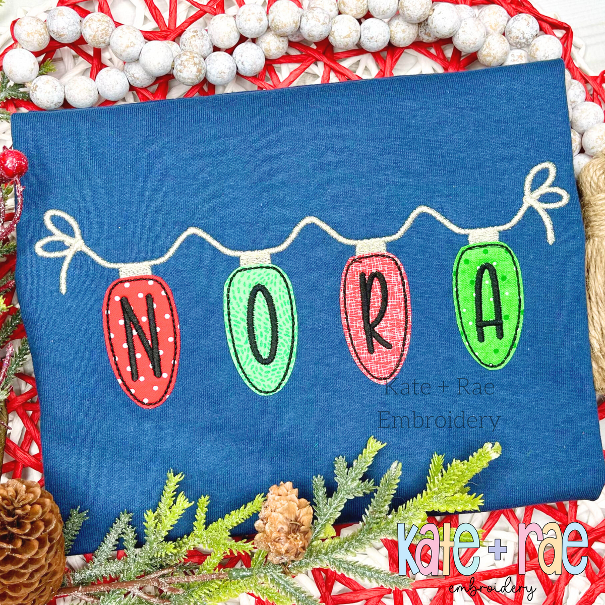 Christmas Lights Bean Stitch Applique Embroidery Font: Christmas light bulbs spelling NORA hanging from a white strand on a navy shirt