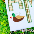 Mallard Duck with Heart Mini Fill Embroidery Design: Small mallard duck holding a red heart beside a green plaid applique monogram on a white shirt