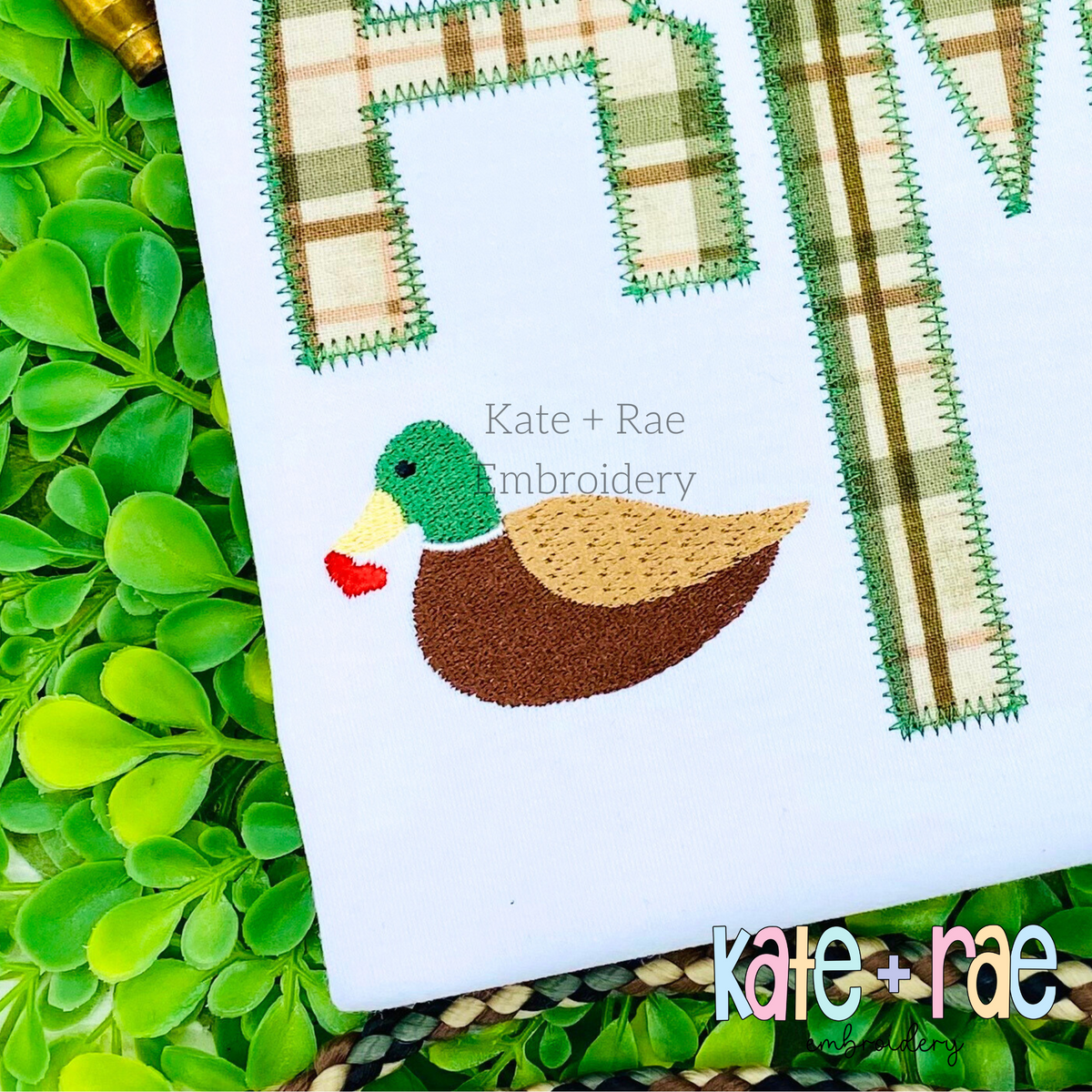 Mallard Duck with Heart Mini Fill Embroidery Design: Small mallard duck holding a red heart beside a green plaid applique monogram on a white shirt