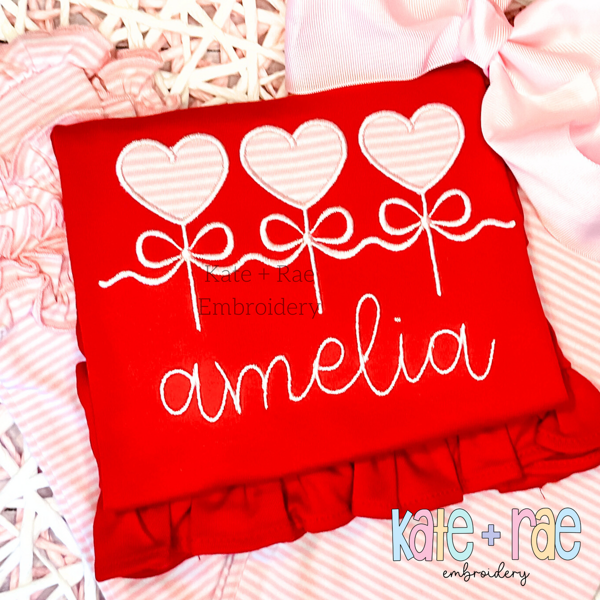Heart Sucker Trio with Bows Satin Stitch Applique Embroidery Design: Three pink striped heart sucker appliques tied with white bows above the name amelia in white script on a red shirt