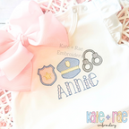 Police Trio Sketch Stitch Embroidery Design: Sketch stitch police badge, hat, and handcuffs above the name Annie on a white shirt with a pink bow