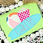 Happy Days Bean Stitch Embroidery Font: The name Callie in pink bean stitch letters on a blue surfboard applique with a beach ball on a green shirt