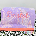 Delilah Outline Satin Stitch Embroidery Font: The name Bristol in pink outline script on a purple seashell print towel