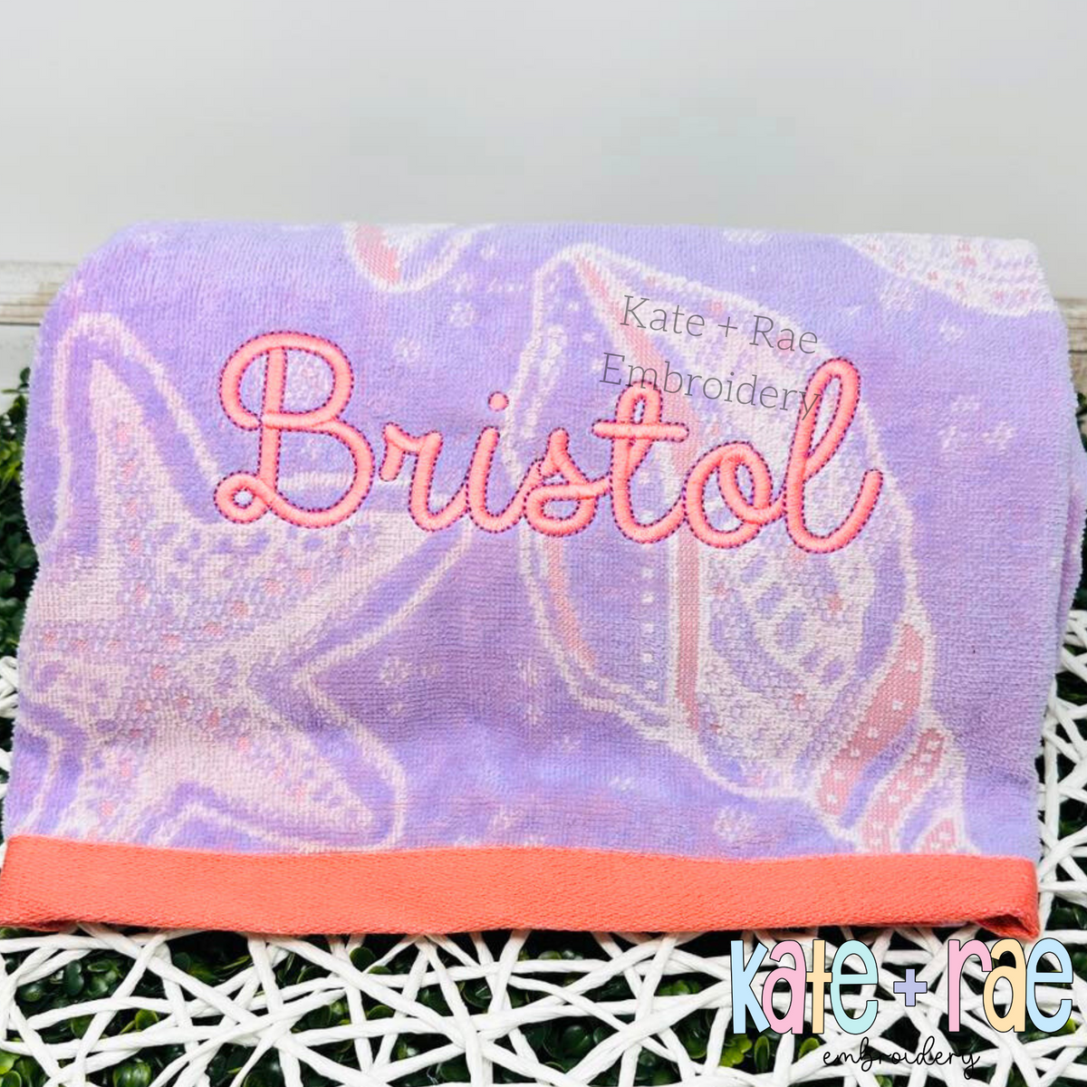 Delilah Outline Satin Stitch Embroidery Font: The name Bristol in pink outline script on a purple seashell print towel
