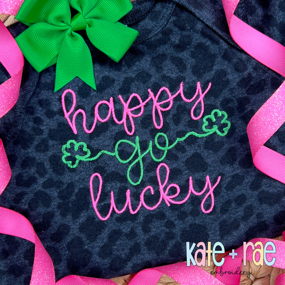 Shamrock Font Add On Embroidery Design: The words happy go lucky in pink script with green shamrock ends on a leopard print shirt