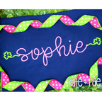 Shamrock Font Add On Embroidery Design: The name sophie in pink script with green shamrock ends on a navy shirt