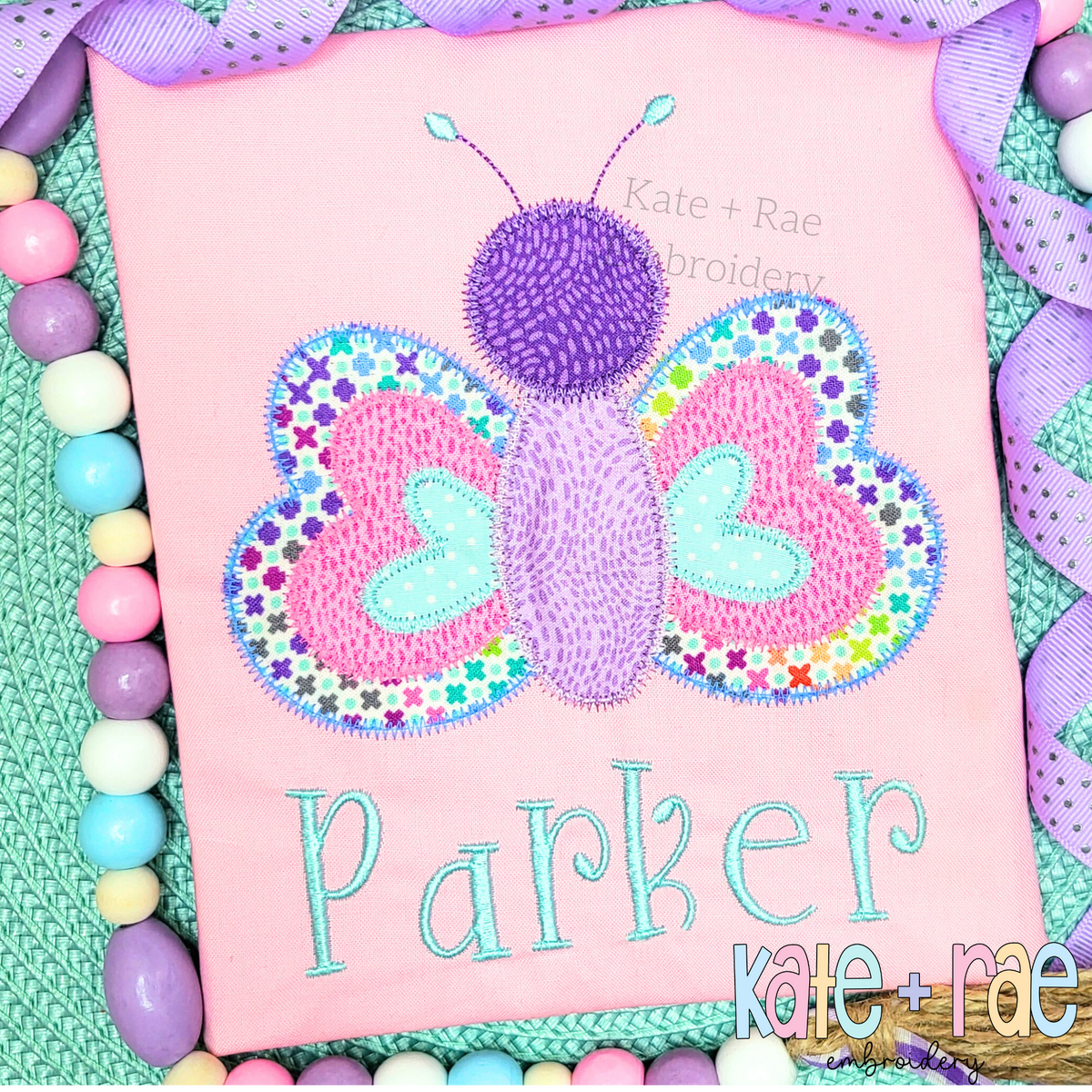 Butterfly Zigzag Stitch Applique Embroidery Design: Patterned pink and purple butterfly zigzag applique above the name Parker in aqua on a pink shirt