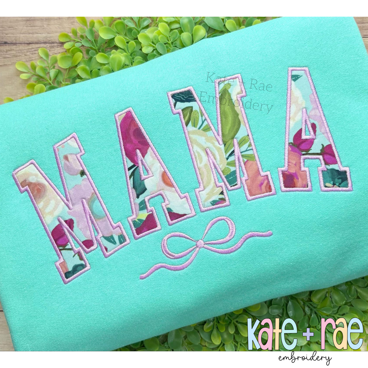 Curved Mama Satin Stitch Applique with Bow Embroidery Design: The word MAMA in pink floral curved collegiate applique letters with a bow on a mint sweatshirt