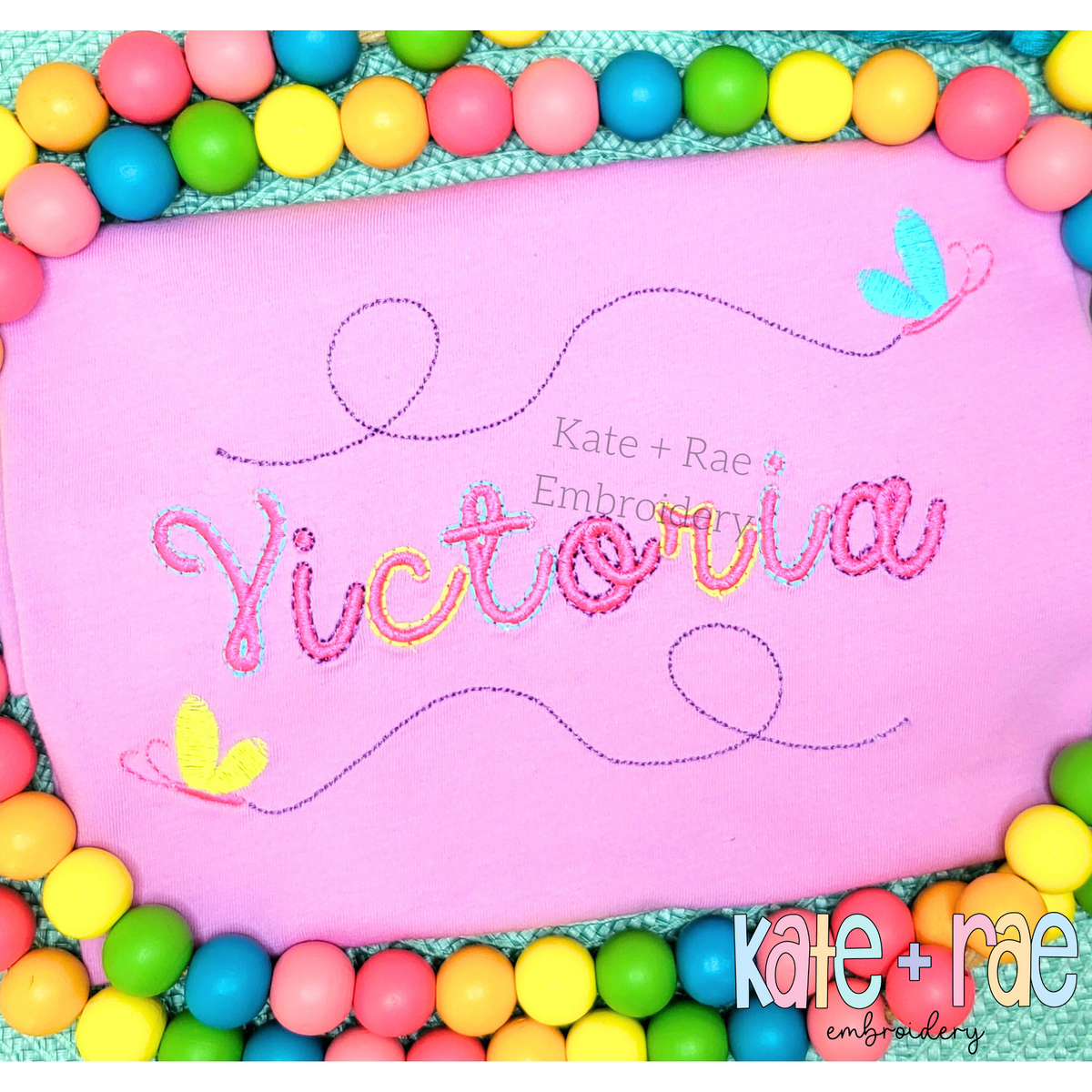 The name Victoria in pastel outline script with butterflies on a pink shirt
