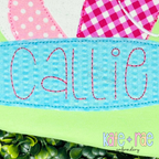 Happy Days Bean Stitch Embroidery Font: Close-up of the name Callie in pink bean stitch on a blue seersucker surfboard applique