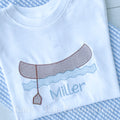 Canoe Sketch Stitch Embroidery Design: Brown sketch stitch canoe with a paddle over blue waves above the name Miller stitched on a white shirt