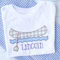 Canoe E-Stitch Applique Embroidery Design: Tan gingham canoe with a paddle over blue waves above the name Lincoln stitched on a white shirt