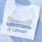 Canoe Zigzag Applique Embroidery Design: Tan gingham canoe with a paddle over blue waves above the name Lincoln stitched on a white shirt