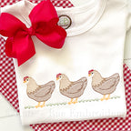 Chicken Trio Sketch Stitch Embroidery Design: Three tan sketch stitch hens in a row on grass stitched on a white shirt with a red bow