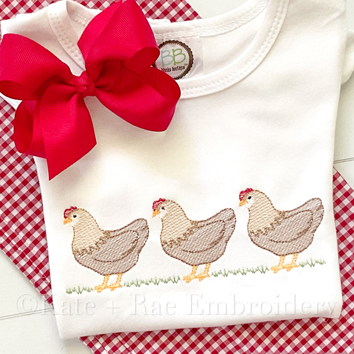 Chicken Trio Sketch Stitch Embroidery Design: Three tan sketch stitch hens in a row on grass stitched on a white shirt with a red bow
