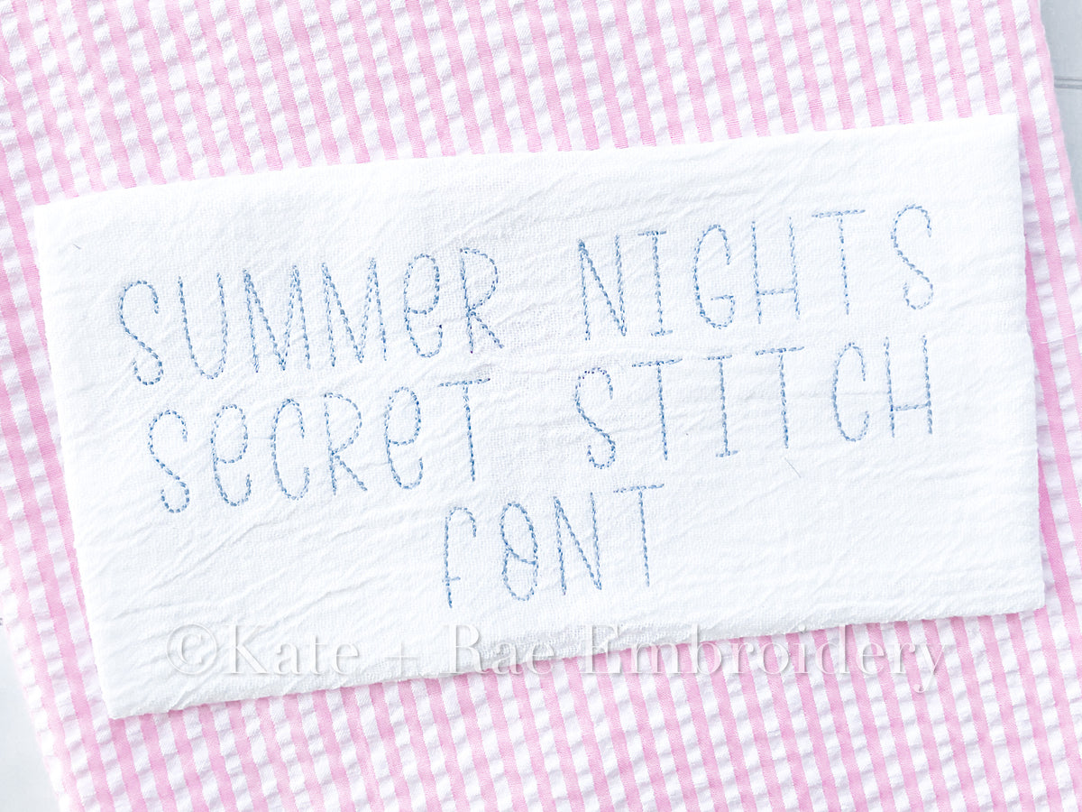 Summer Nights Secret Stitch Embroidery Font: The words Summer Nights Secret Stitch Font stitched in light gray on white fabric over pink gingham