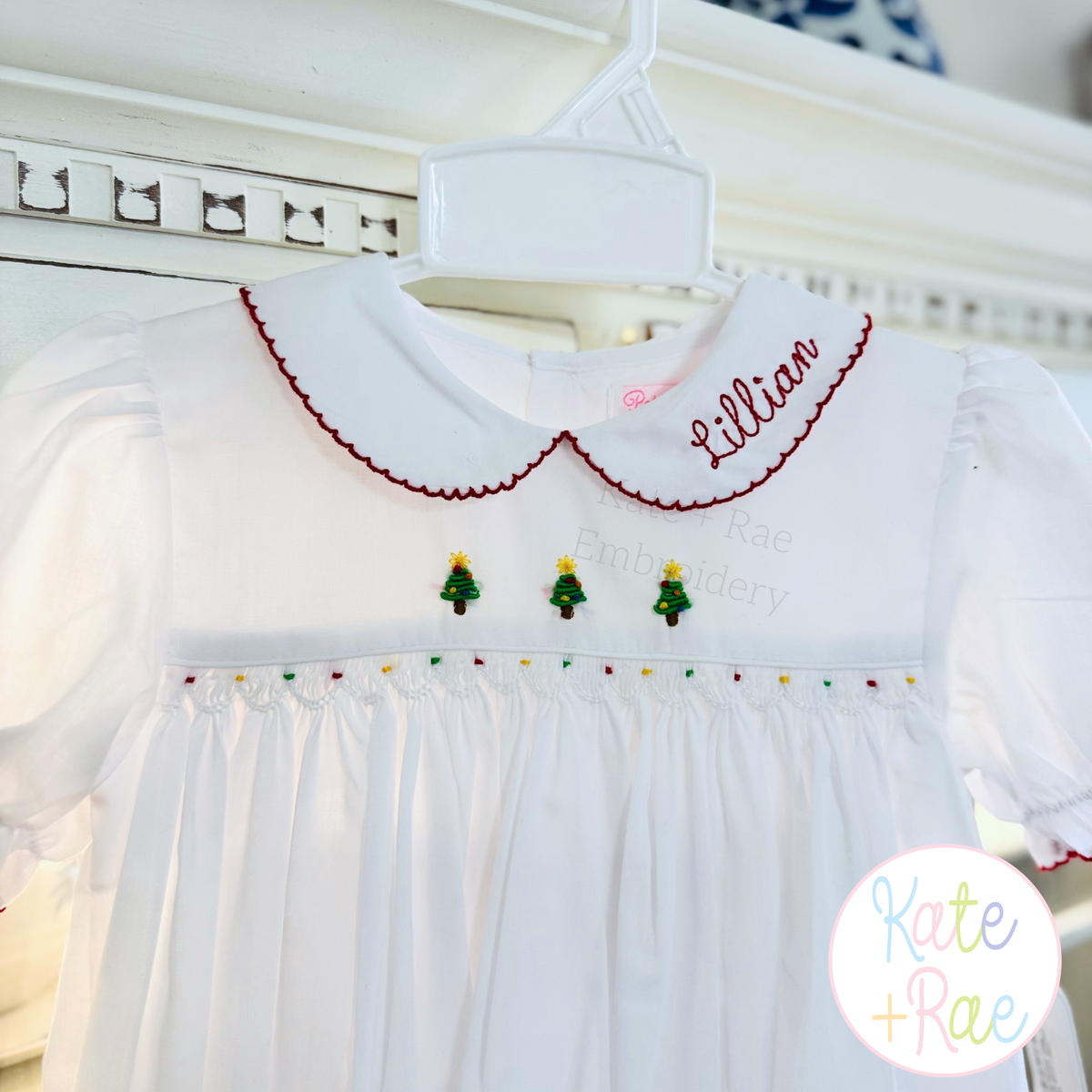 Delilah Bean Stitch Embroidery Font: The name Lillian in red bean stitch script on the collar of a white smocked Christmas dress