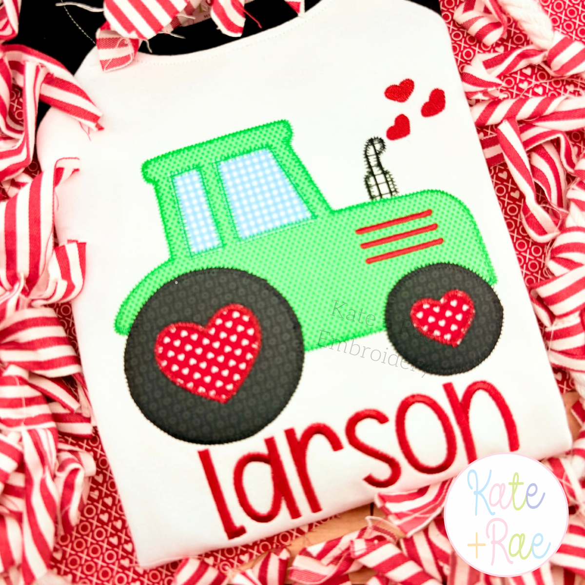 Valentine's Day Heart Tractor Zigzag Applique Embroidery Design: Green tractor applique with red heart wheels above the name larson in red on a white shirt