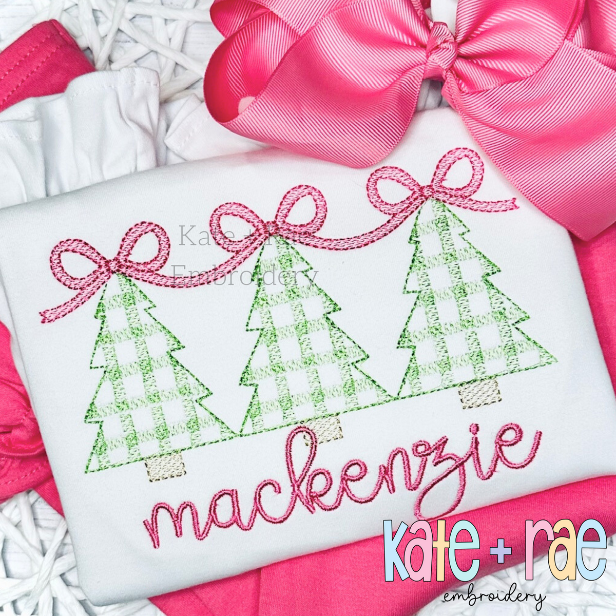 Girls Plaid Christmas Tree Trio with Connecting Bows Sketch Stitch Embroidery Design: Three green plaid Christmas trees linked by pink bows above the name mackenzie in pink script on a white shirt