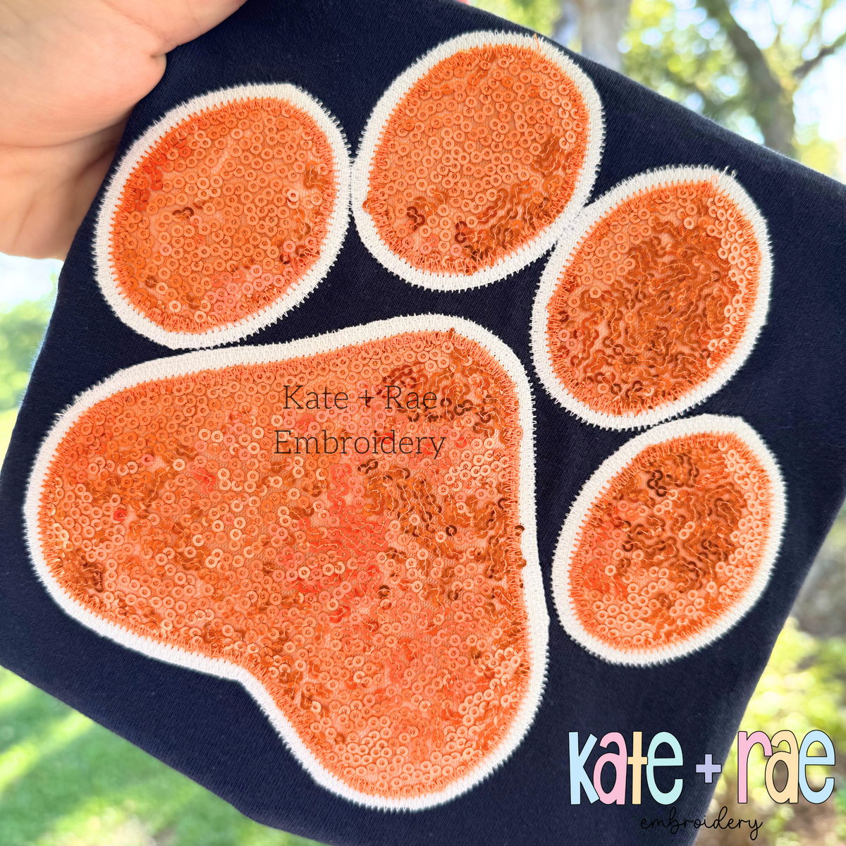 Paw Print Double Zigzag Stitch Applique Embroidery Design: Orange sequin paw print applique with white outline on a navy shirt
