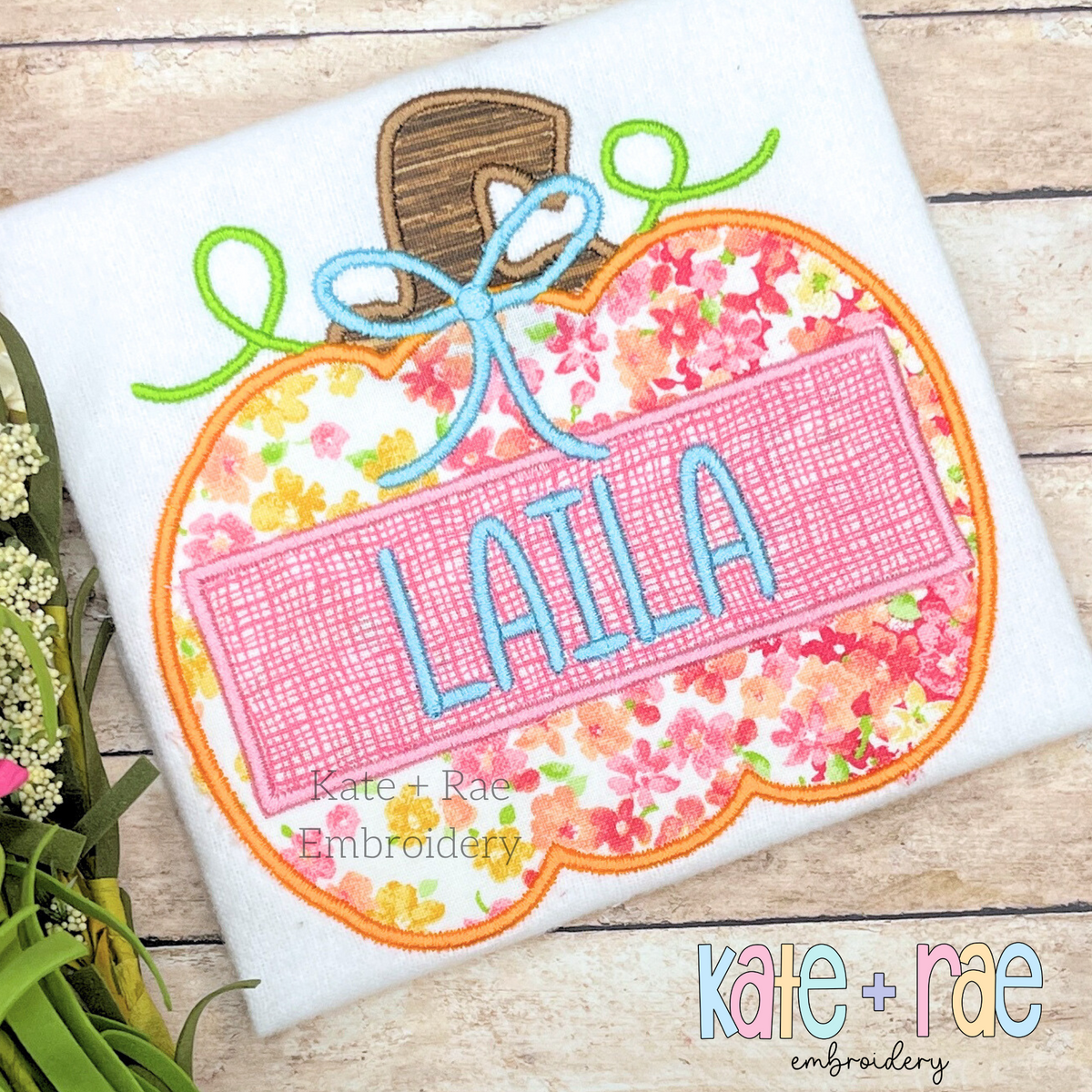 Girl's Pumpkin Satin Applique Embroidery Design: Pink floral pumpkin applique with a bow and the name LAILA on a white shirt