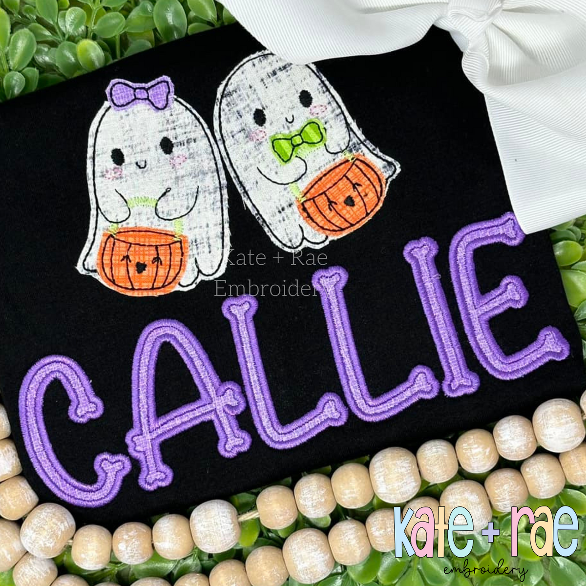Bones Satin Stitch Applique Embroidery Font: Two ghosts holding jack-o-lantern buckets above the name CALLIE in purple applique letters on a black shirt