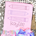 Pencil Trio Outline Bean Stitch Embroidery Design: Three outline pencils in pink, purple, and blue above the name Kaylee on a pink shirt