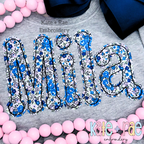Dottie Bean Stitch Applique Embroidery Font: The name Mila in blue floral bean stitch applique letters on a gray sweatshirt