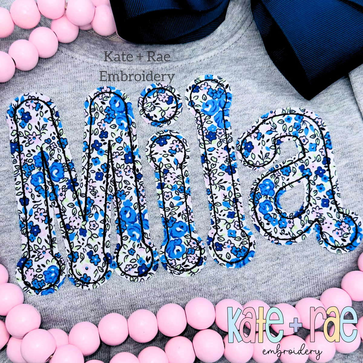 Dottie Bean Stitch Applique Embroidery Font: The name Mila in blue floral bean stitch applique letters on a gray sweatshirt