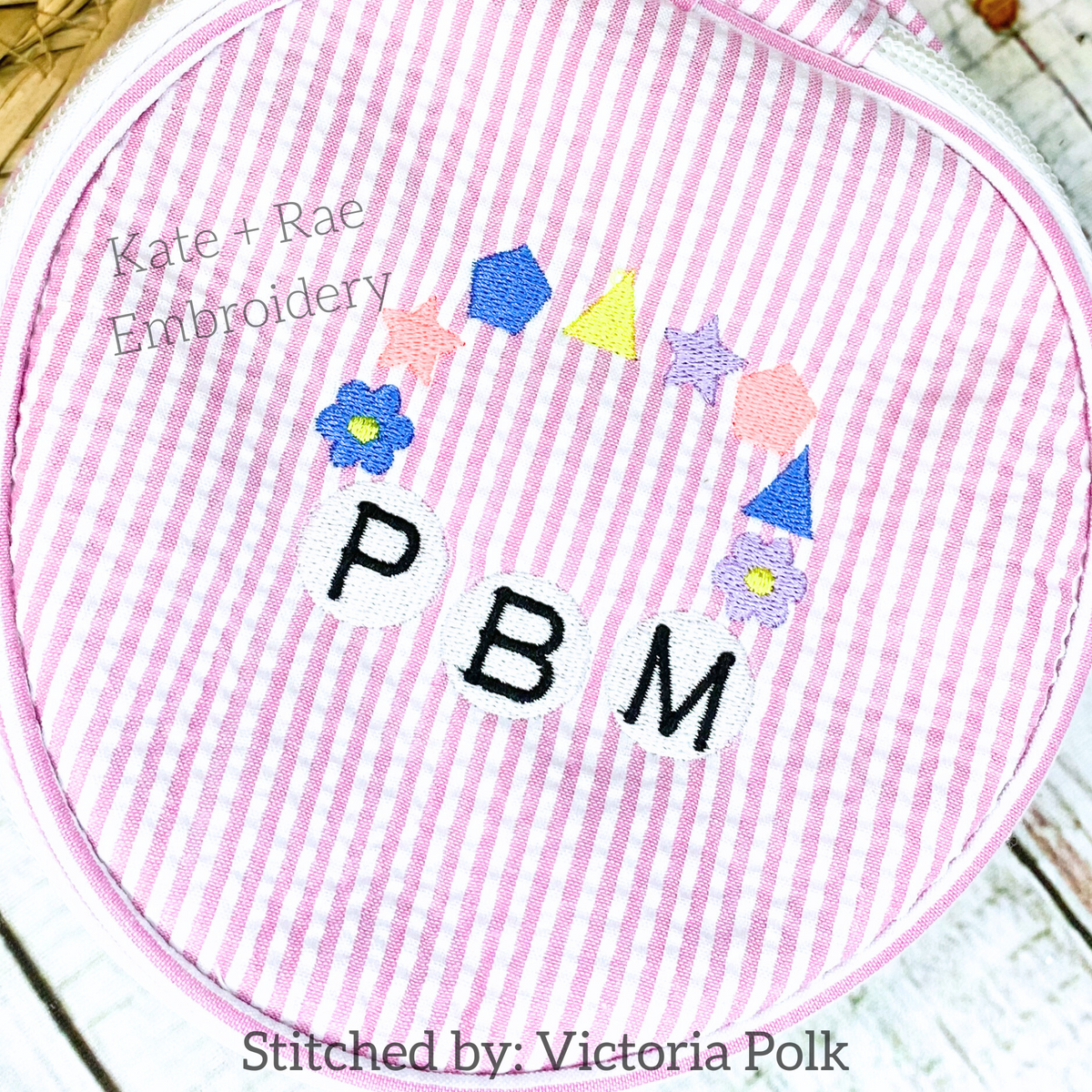 Friendship Embroidery Font: Friendship bracelet arc of bead shapes above the letters PBM on a pink seersucker bag