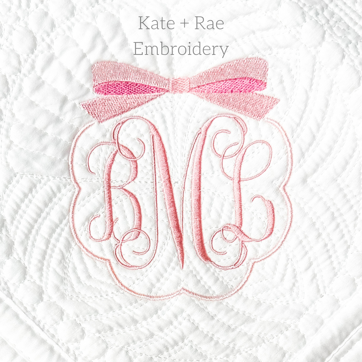 Scalloped Monogram Frame with Bow Embroidery Design: Pink scalloped frame with a pink bow around a script monogram on a white quilted blanket